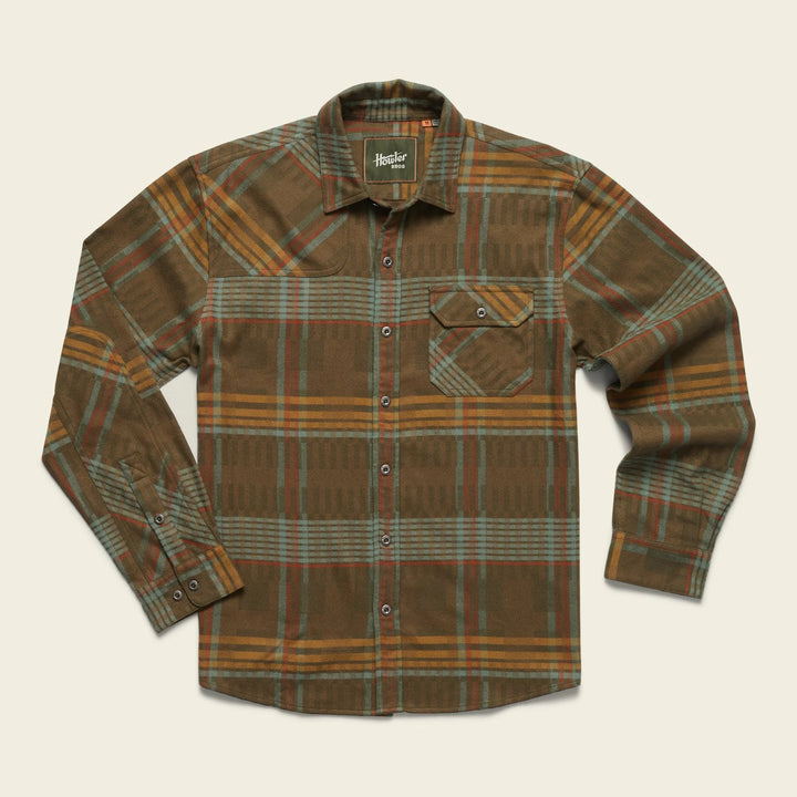 A long-sleeved plaid flannel shirt with a button-through flap pocket on the left chest, reinforced elbow patches, and custom metal buttons.