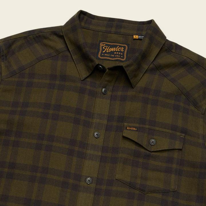 Green Howler Brothers plaid shirt with a brand logo on a beige background