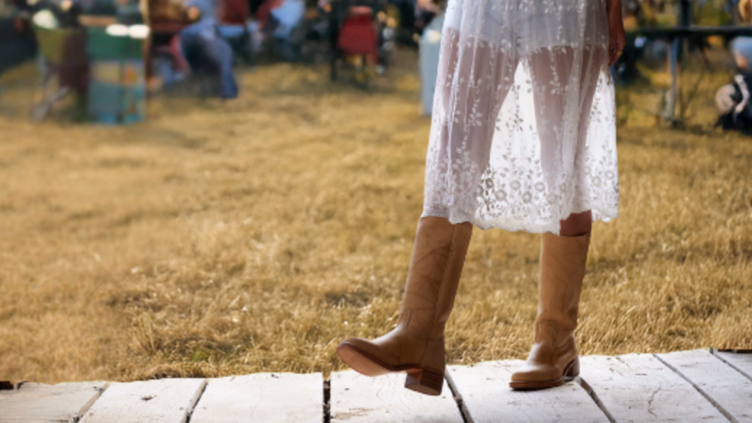 A woman wearing Frye campus boots with grass and people sitting around tables in the background