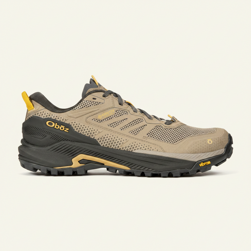 A single Oboz hiking shoe in a tan and black colorway with yellow accents, shown in a side profile against a solid green background.