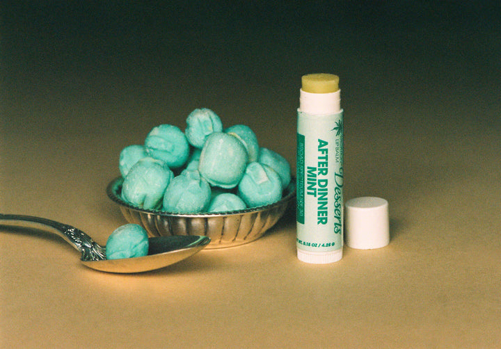 Teal candies in a bowl with a spoon, a stick of after dinner mint candy, and a container on a beige background.