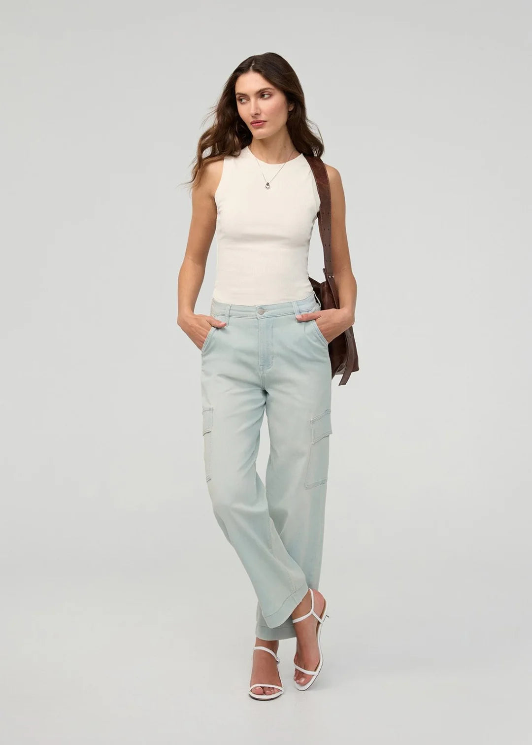 Woman wearing a white sleeveless top and light blue jeans on a gray background
