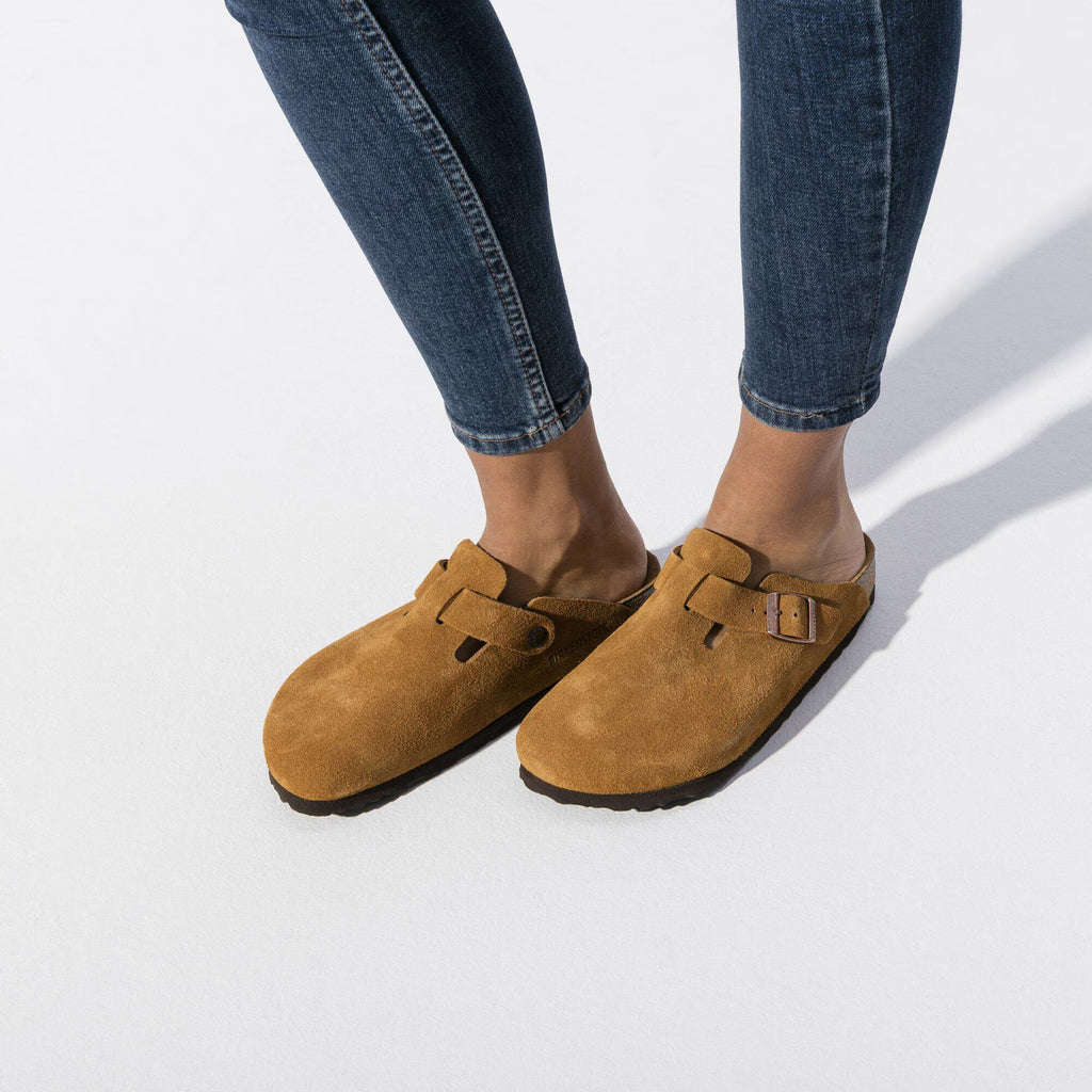Pair of Brown suede clogs with a buckle on a white background worn by a woman