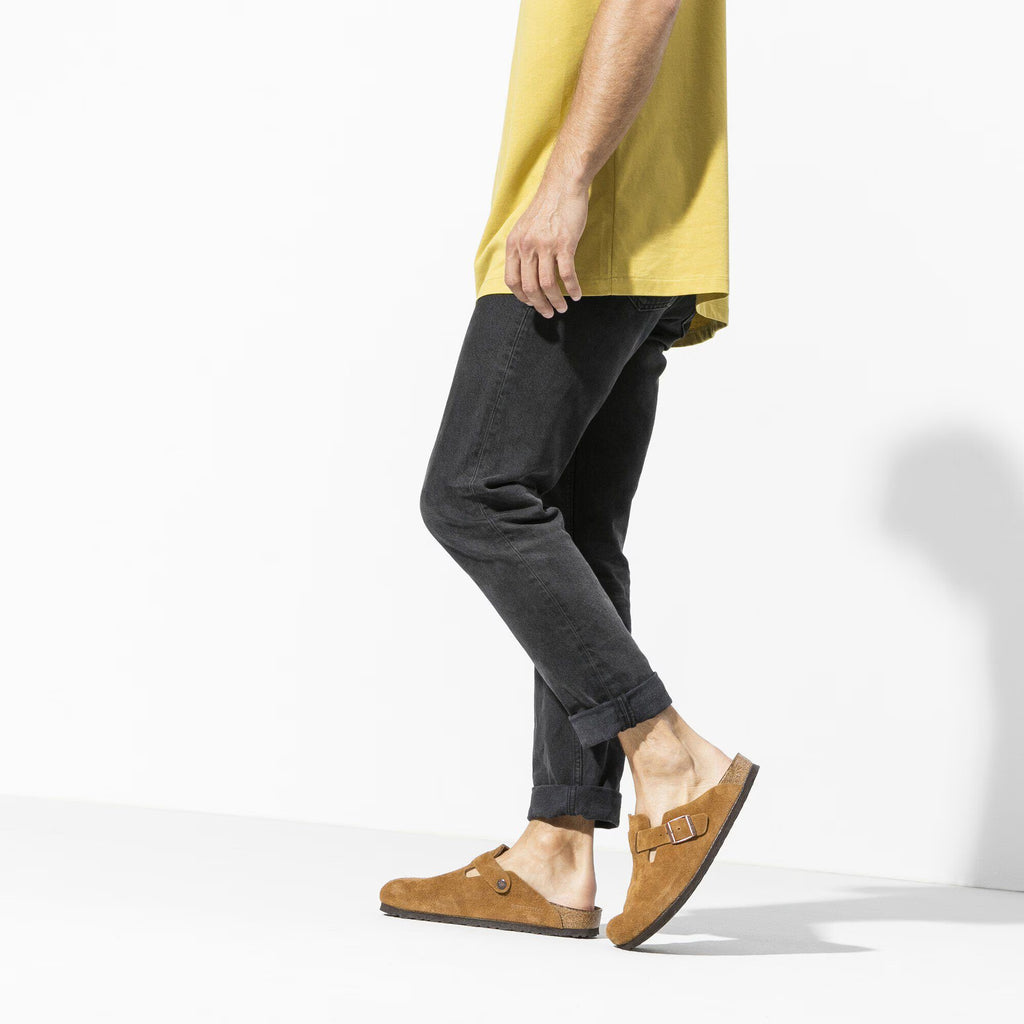 Pair of Brown suede clogs with a buckle on a white background worn by a model