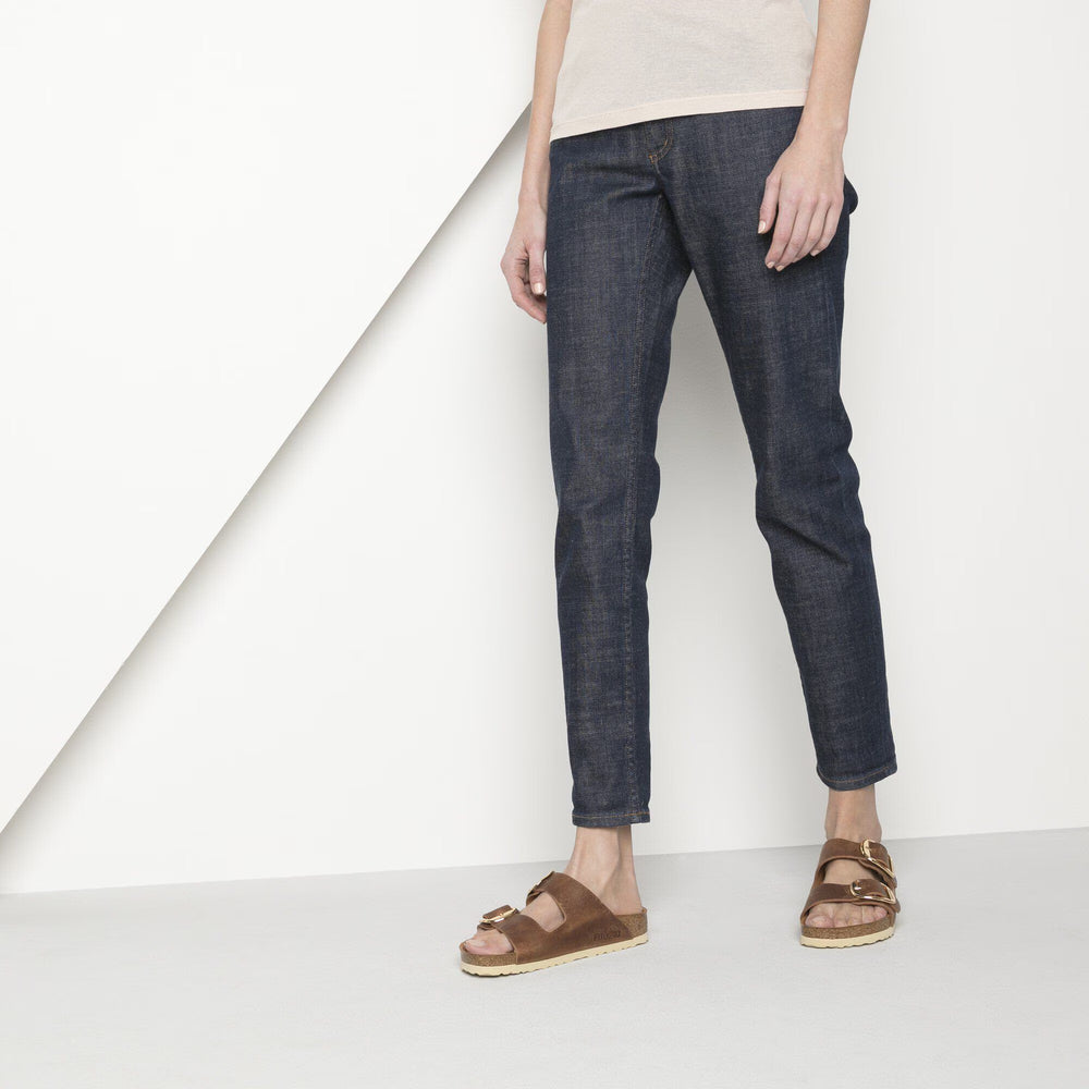 Person wearing dark blue jeans and brown sandals on a white background