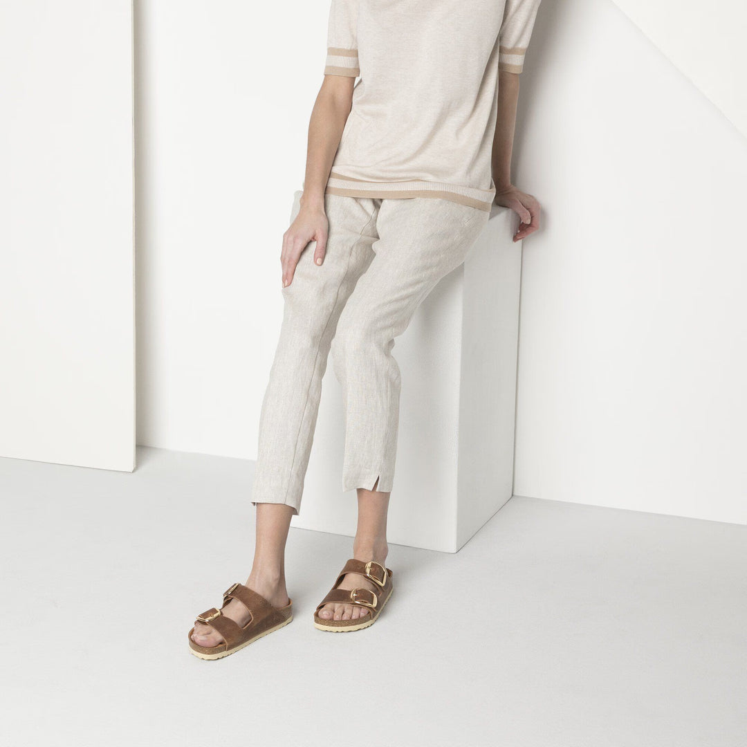 Person wearing beige pants and brown sandals against a white background