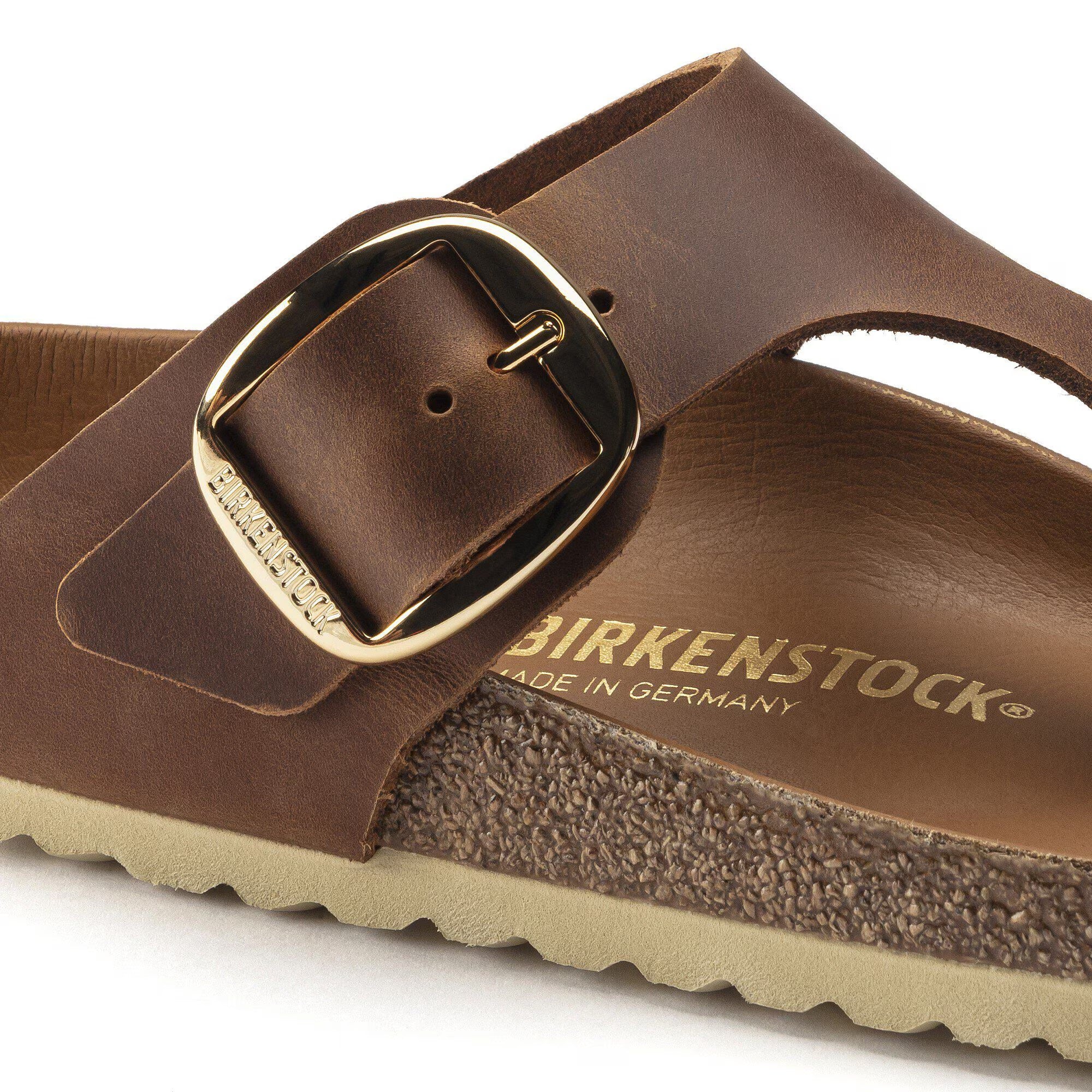 Brown sandal with gold buckle and 'Birkenstock' branding on a white background