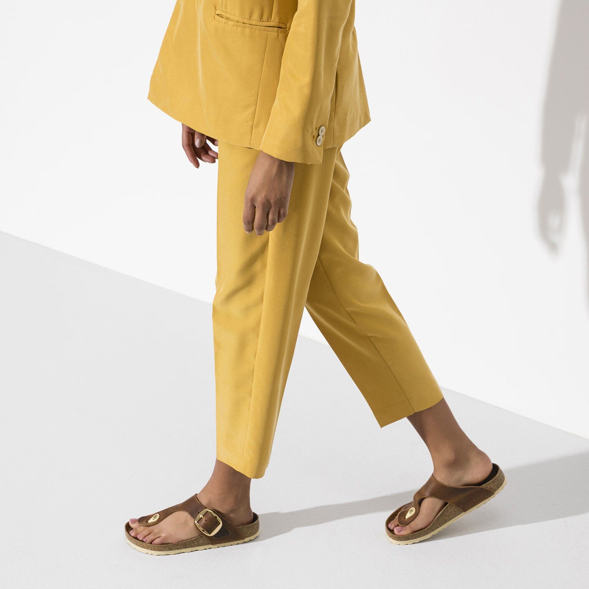 Person wearing a yellow outfit with brown sandals on a white background