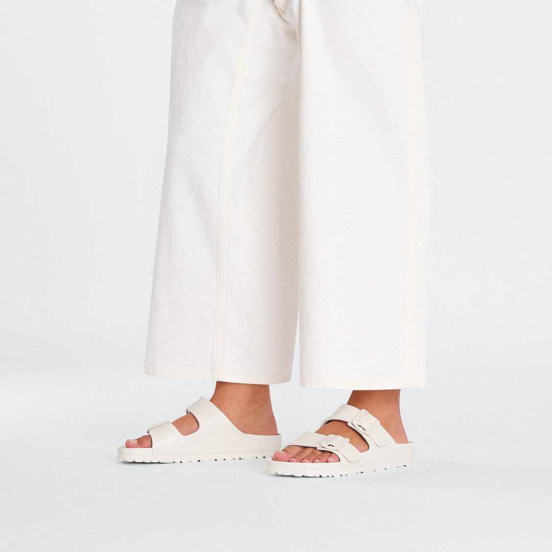 White sandals worn with white pants on a light gray background