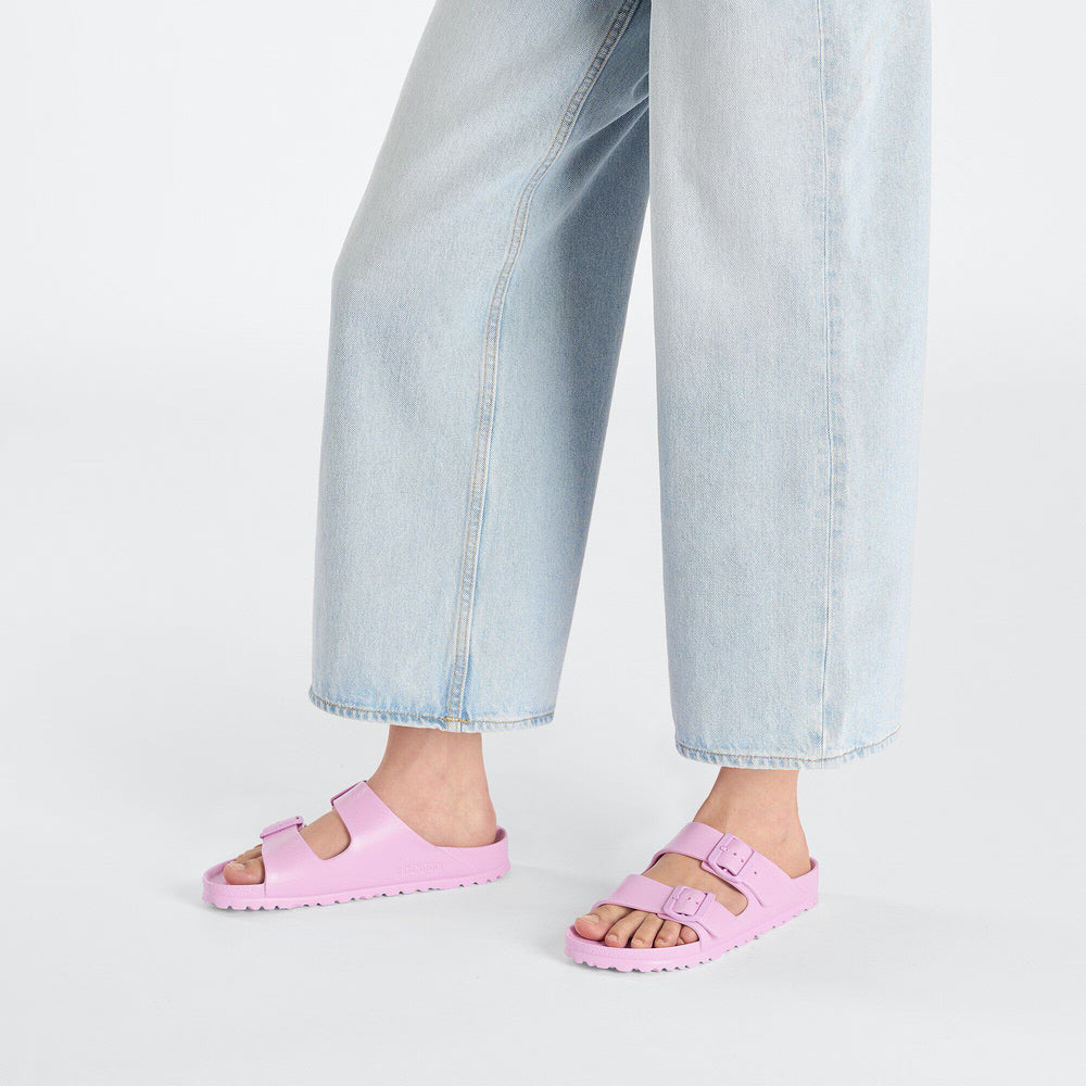 Person wearing pink sandals with light blue jeans on a white background