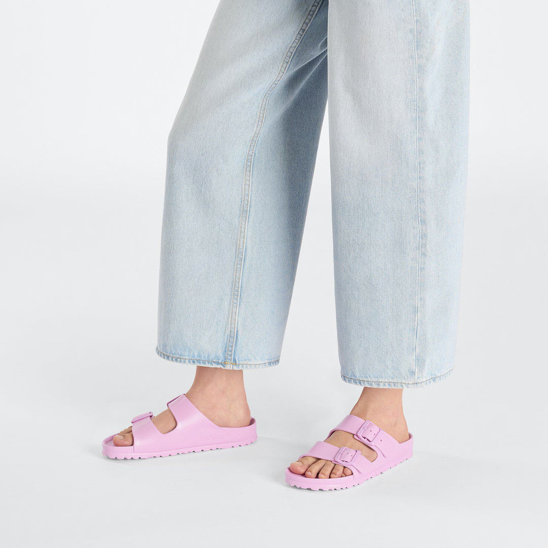 Person wearing pink sandals with light blue jeans on a white background