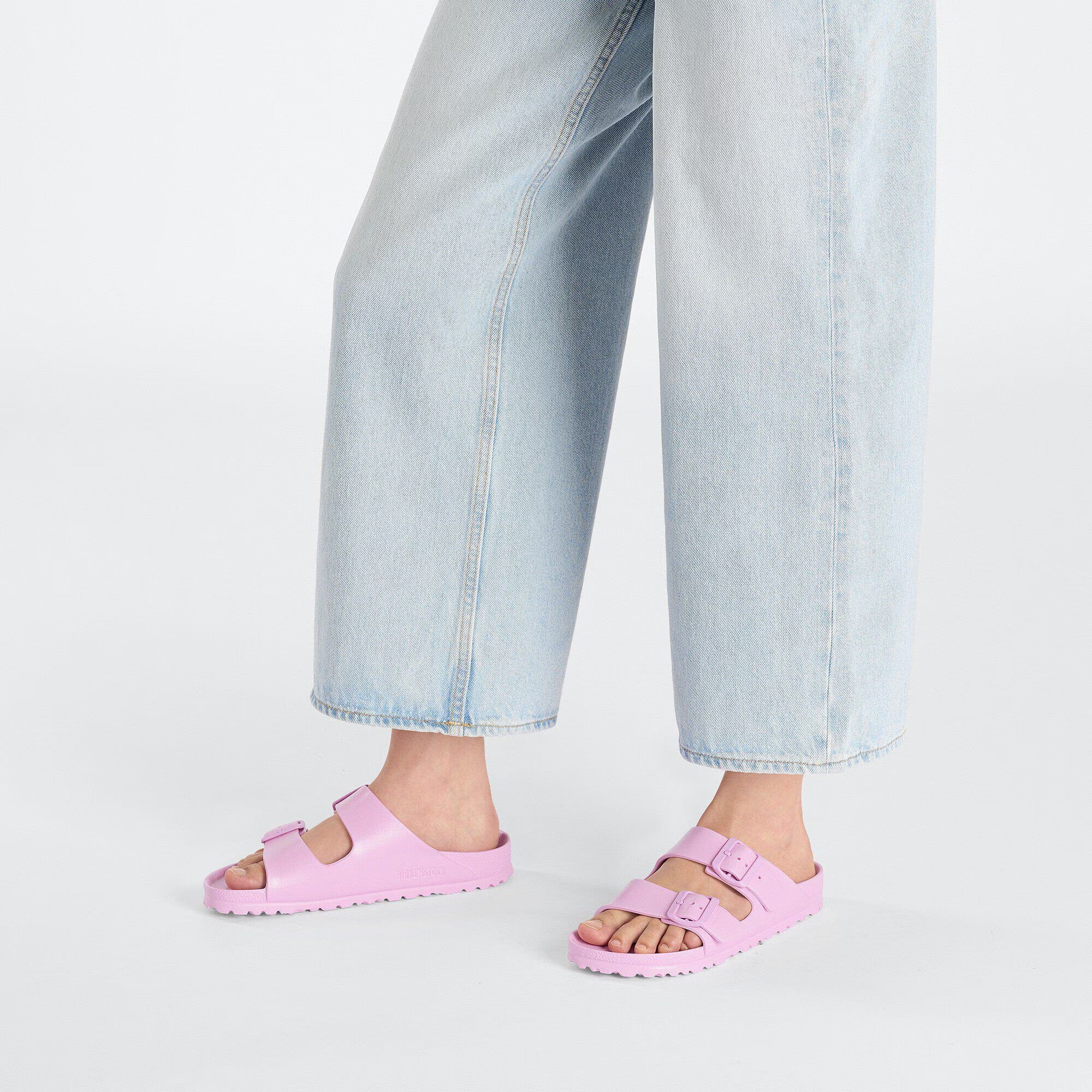 Person wearing pink sandals with light blue jeans on a white background