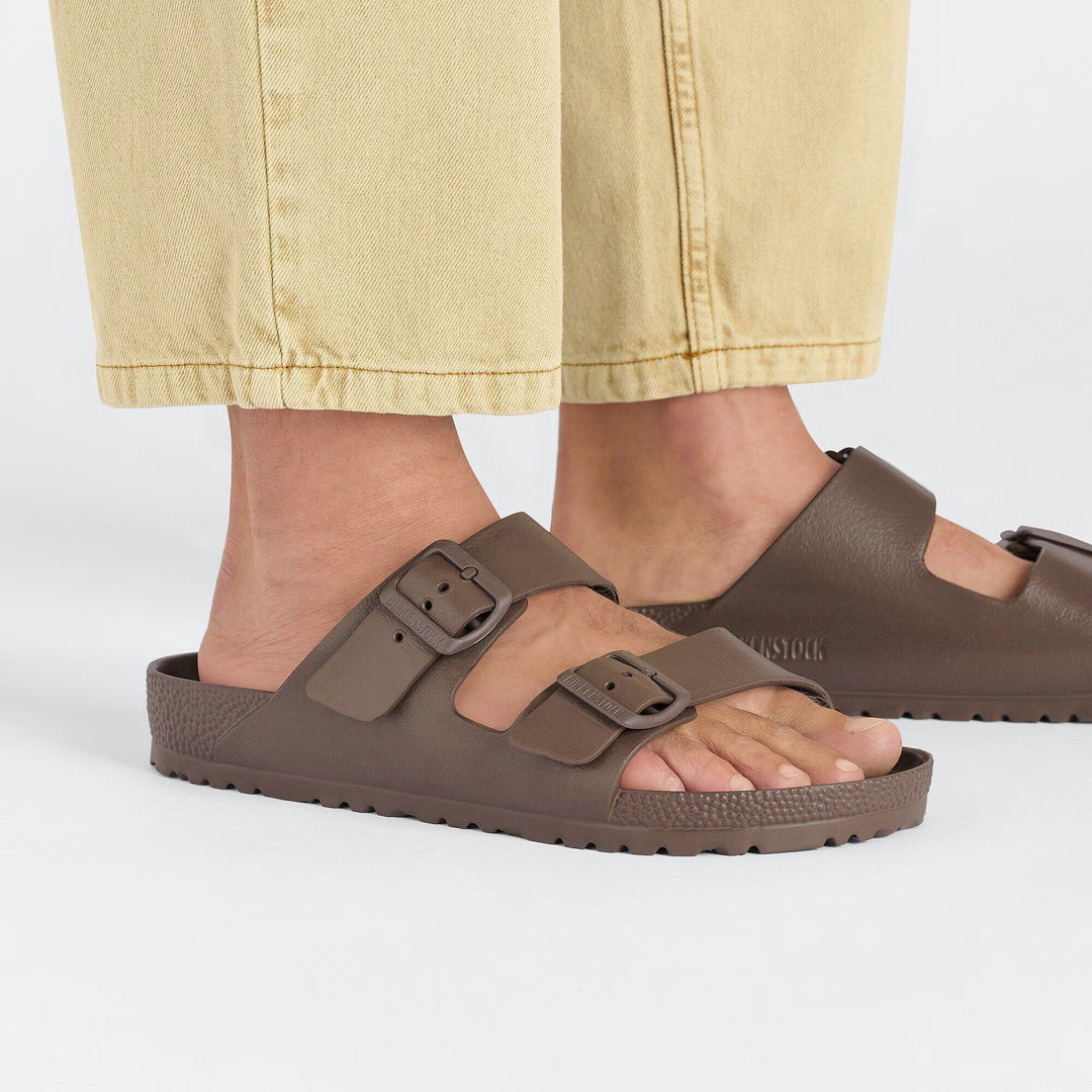 Brown sandals with buckles worn by a person on a white background