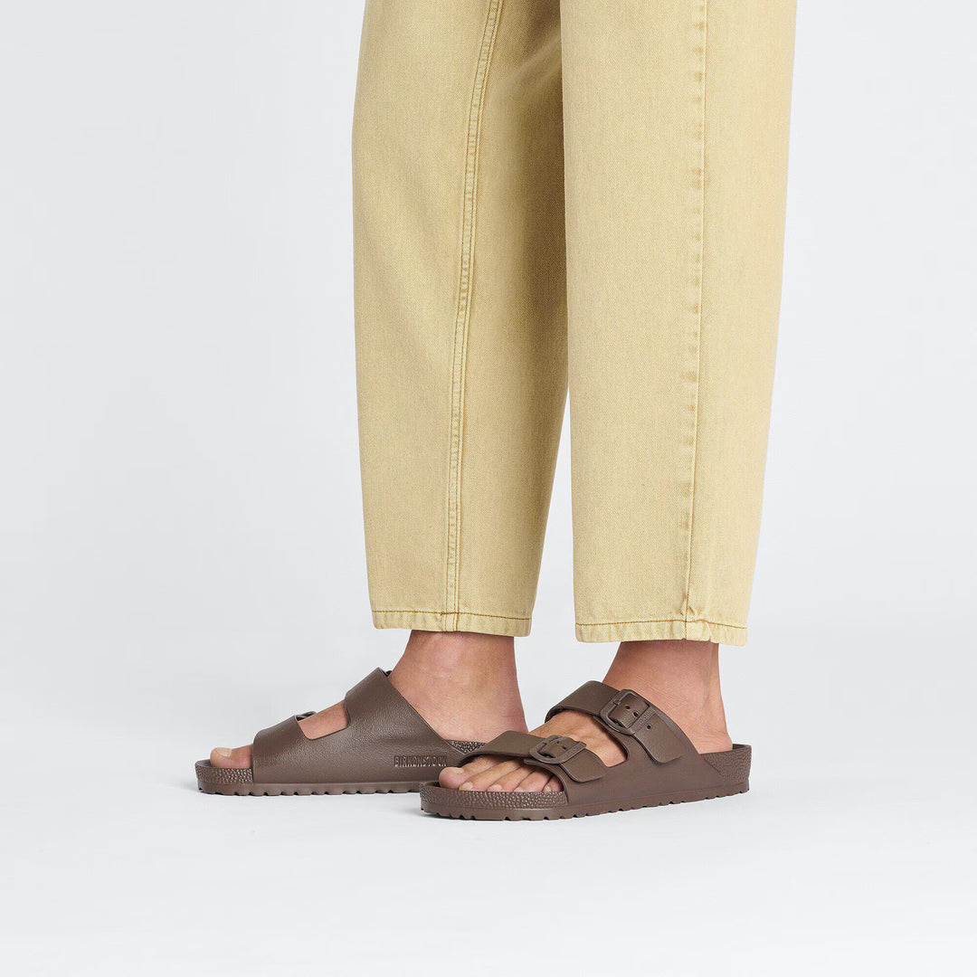Brown sandals worn with beige pants on a light gray background