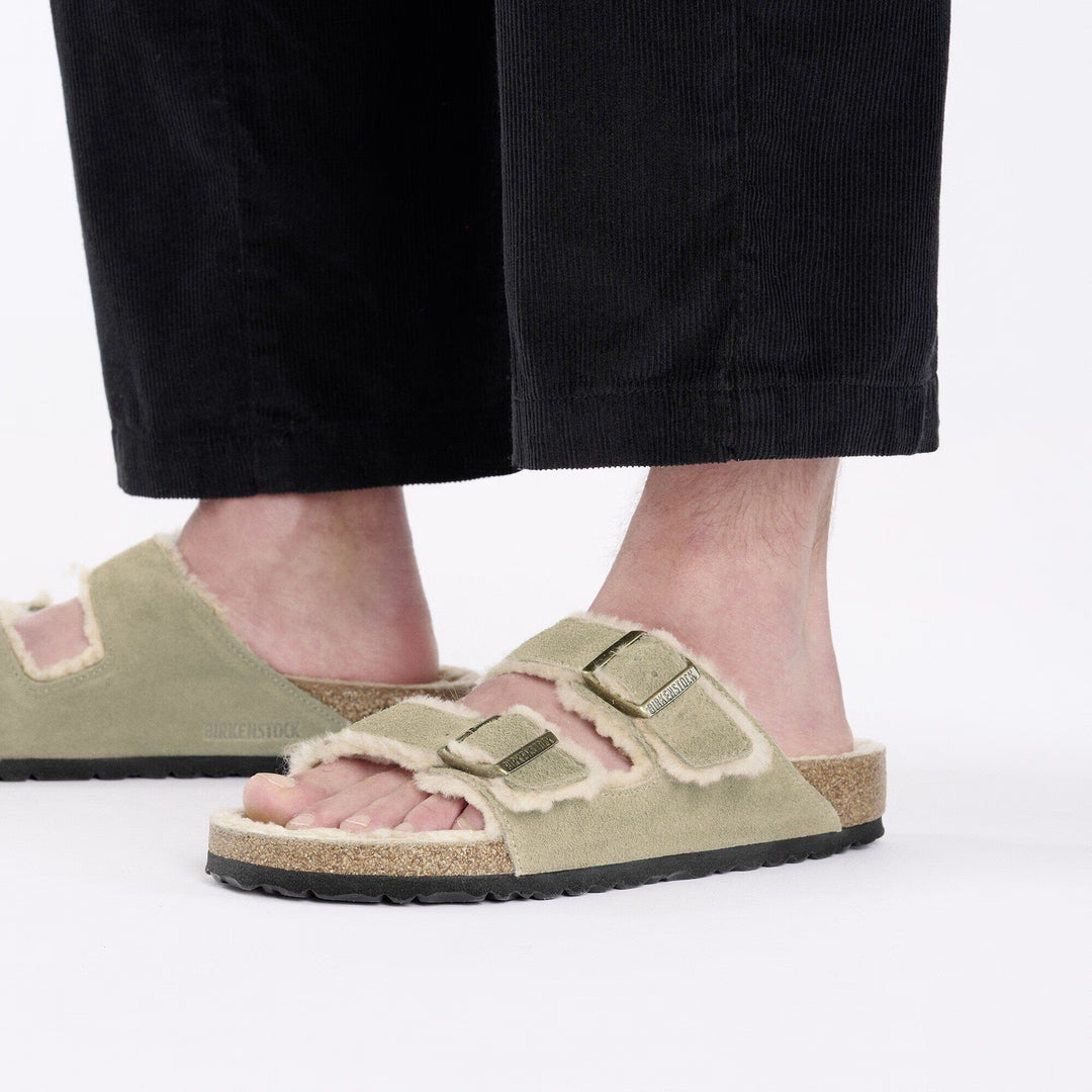 Person wearing green suede sandals with shearling lining on a white background