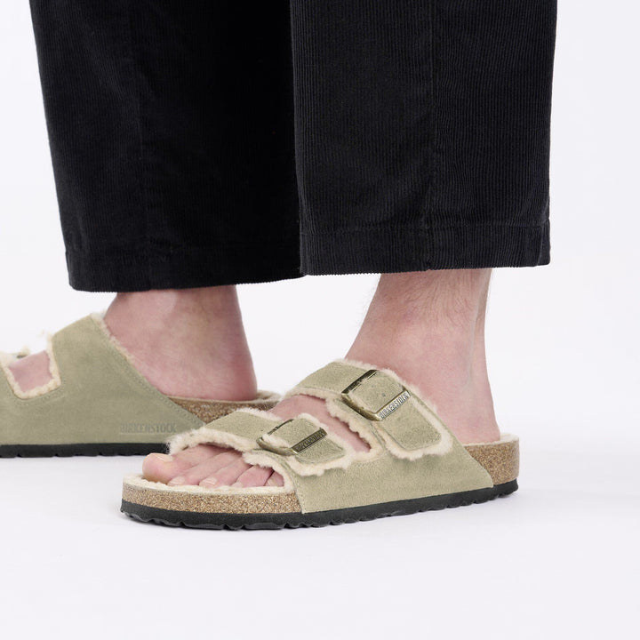 Person wearing green suede sandals with shearling lining on a white background