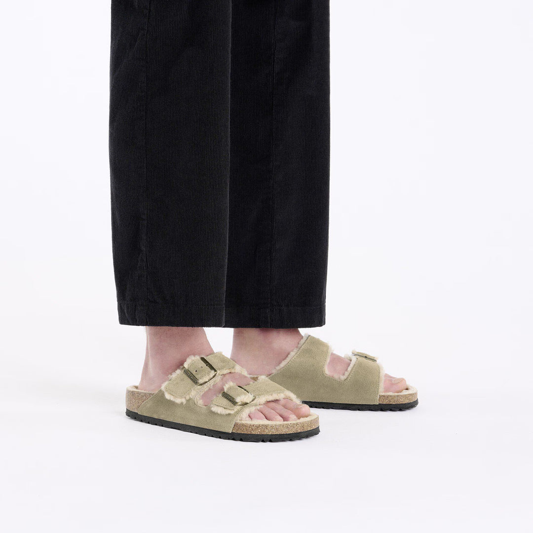 Person wearing beige sandals with black straps on a white background