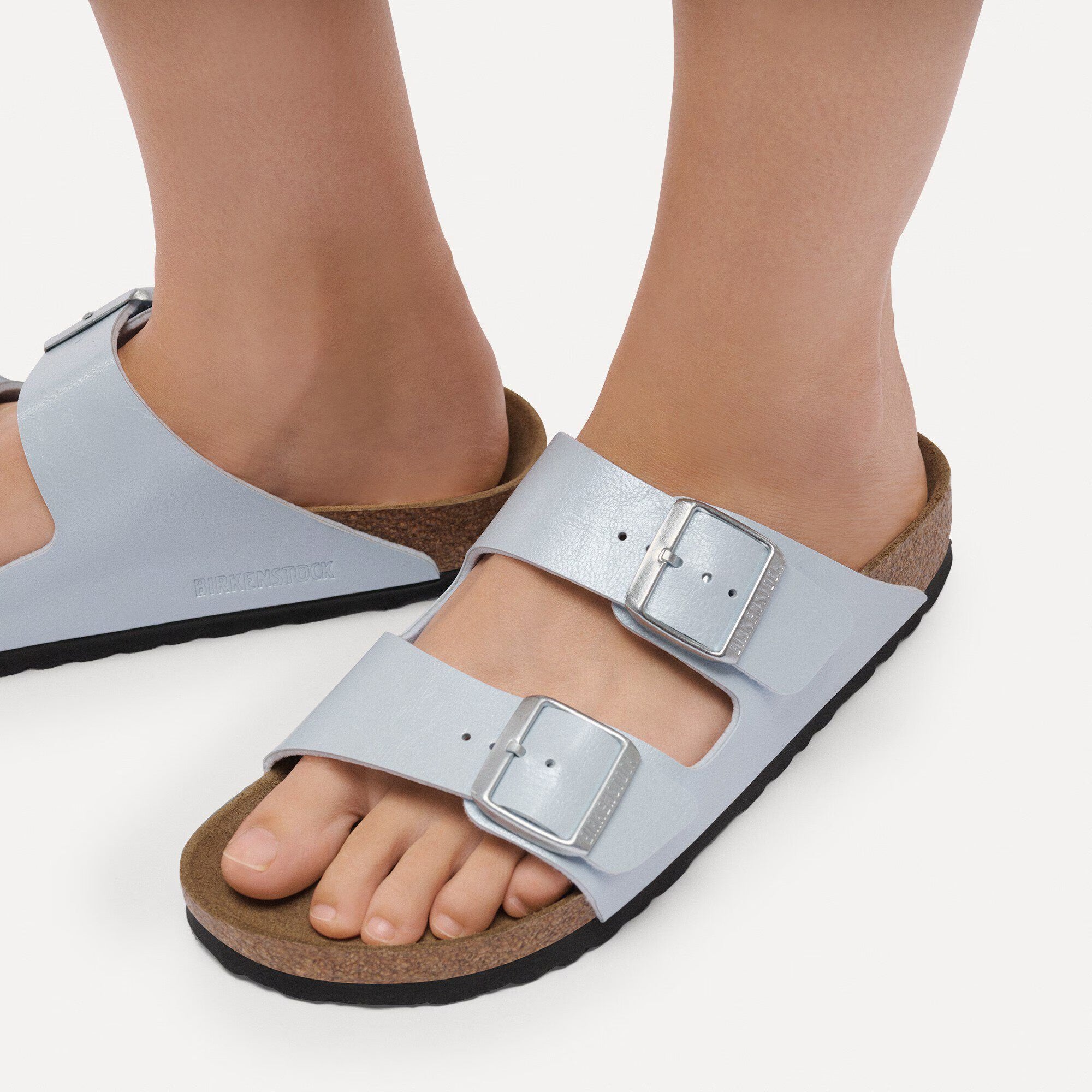 Light blue sandals with buckles worn by a person on a white background