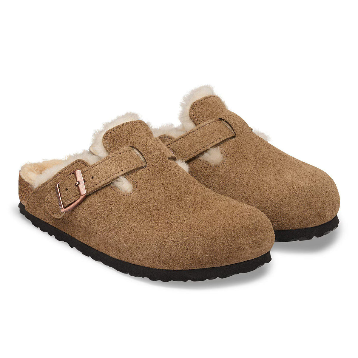 A pair of tan suede clogs with white shearling lining and a small pink buckle detail, shown on a white background.
