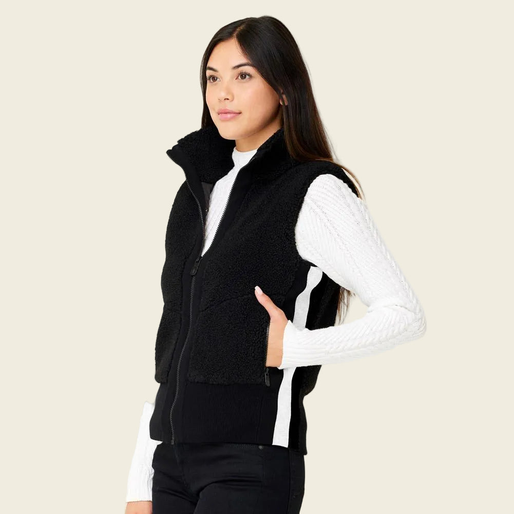 Woman wearing a black vest over a white long-sleeve shirt on a beige background