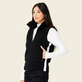 Woman wearing a black vest over a white long-sleeve shirt on a beige background
