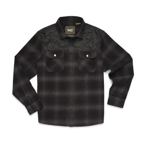 A black and dark gray plaid long-sleeve button-up shirt with a quilted yoke on the chest, featuring two buttoned flap pockets on a white background.
