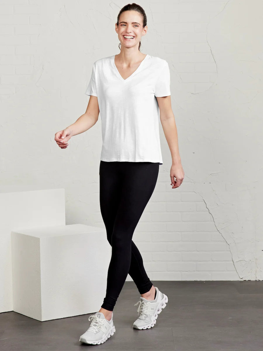 Woman wearing a white t-shirt, black leggings, and white sneakers in a minimalistic setting.