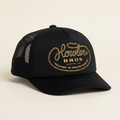 A black trucker-style cap with a curved brim and black mesh back panels, featuring a gold embroidered logo on the front that reads 'Howler Bros. Austin, TX' with 'Welcome to Howler County' below, shown on a plain white background.