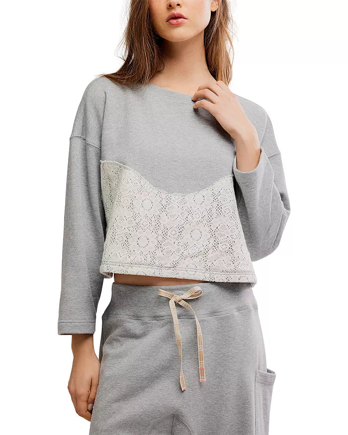 A woman wearing a light gray cropped sweatshirt with a white lace panel across the front and matching gray drawstring sweatpants, shown against a plain white background.