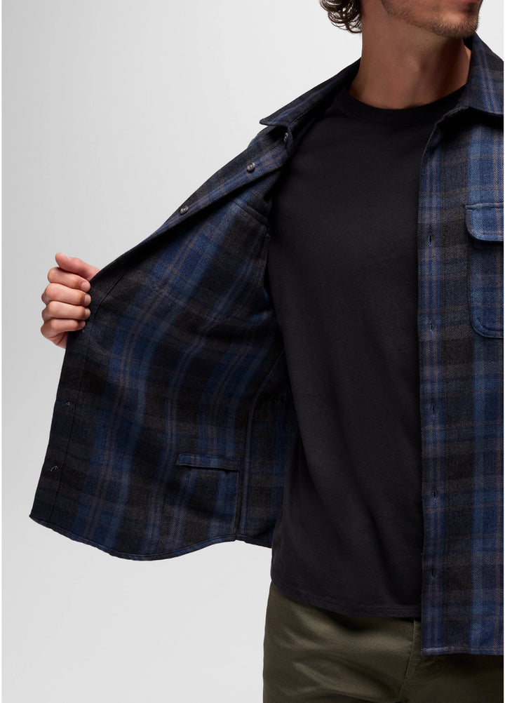 Person wearing a black t-shirt with a blue plaid shirt over it on a plain background