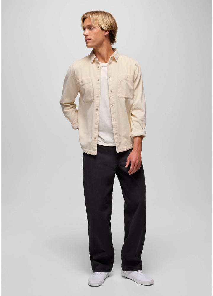 Man wearing a beige shirt over a white shirt with black pants on a plain background