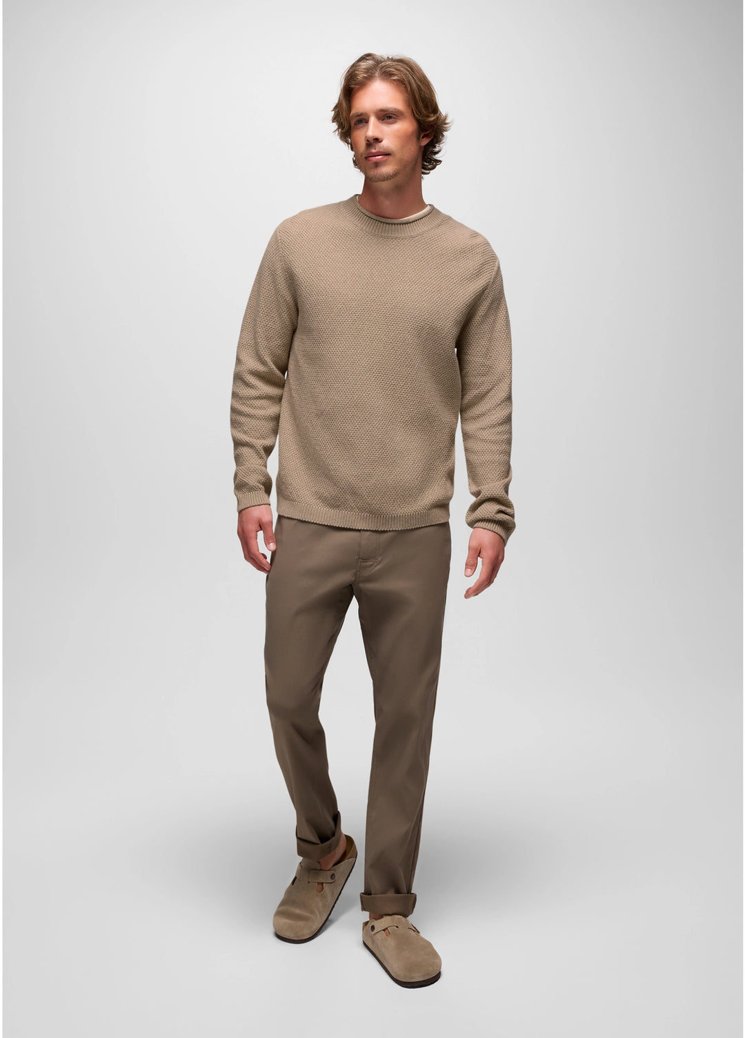 Man wearing a beige sweater and pants on a white background