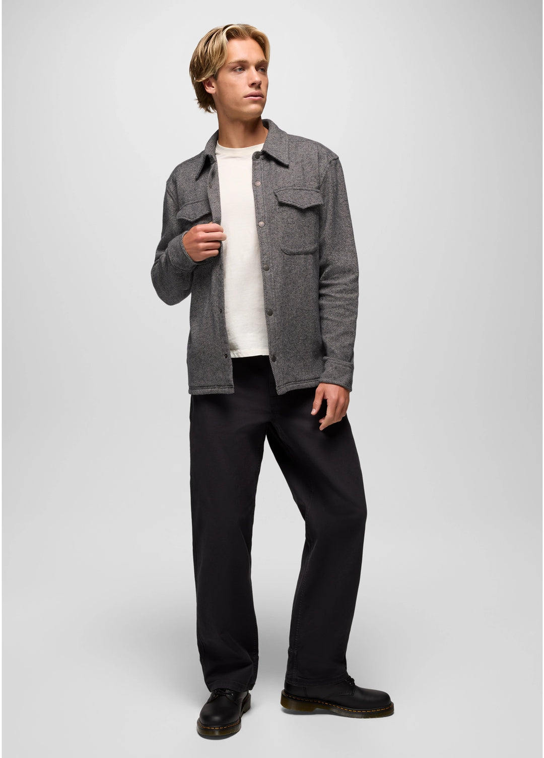 Man wearing a gray jacket, white shirt, black pants, and black shoes on a light gray background