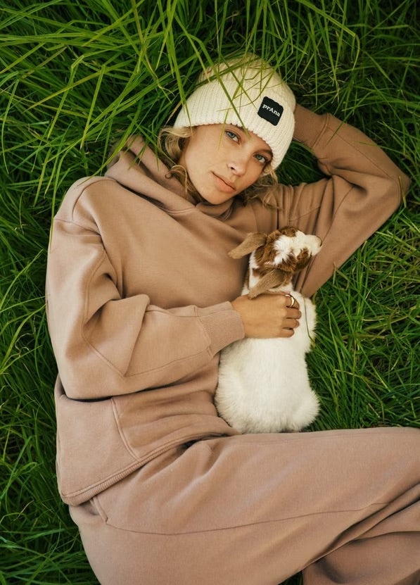 Person in beige outfit lying on grass holding a small animal