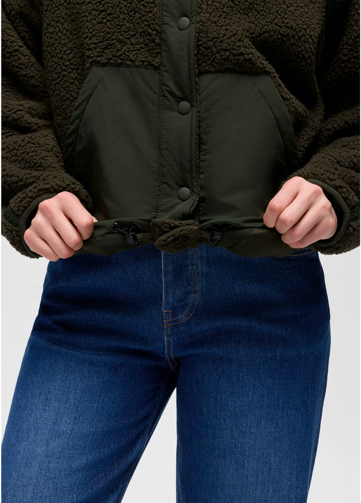 Person wearing a dark green prAna Encinitas Fleece Jacket and blue jeans on a light gray background