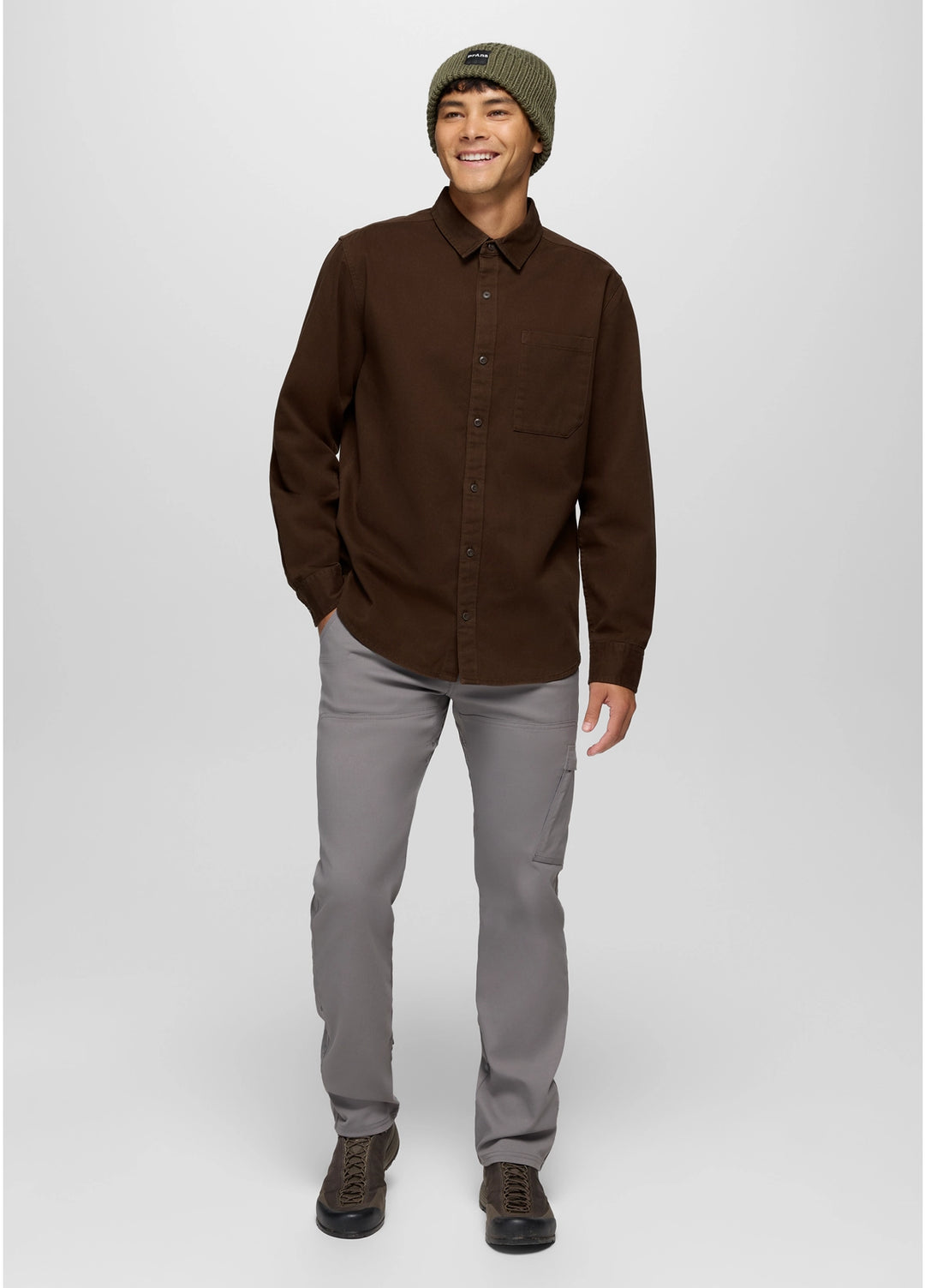 Man wearing a brown shirt, gray pants, and a green beanie on a white background