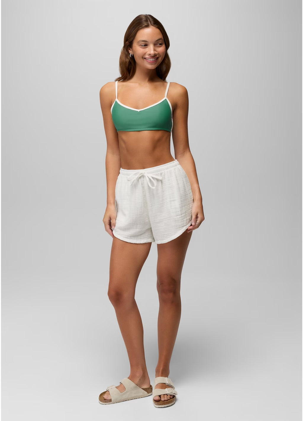 Woman wearing a green sports bra and white shorts on a gray background