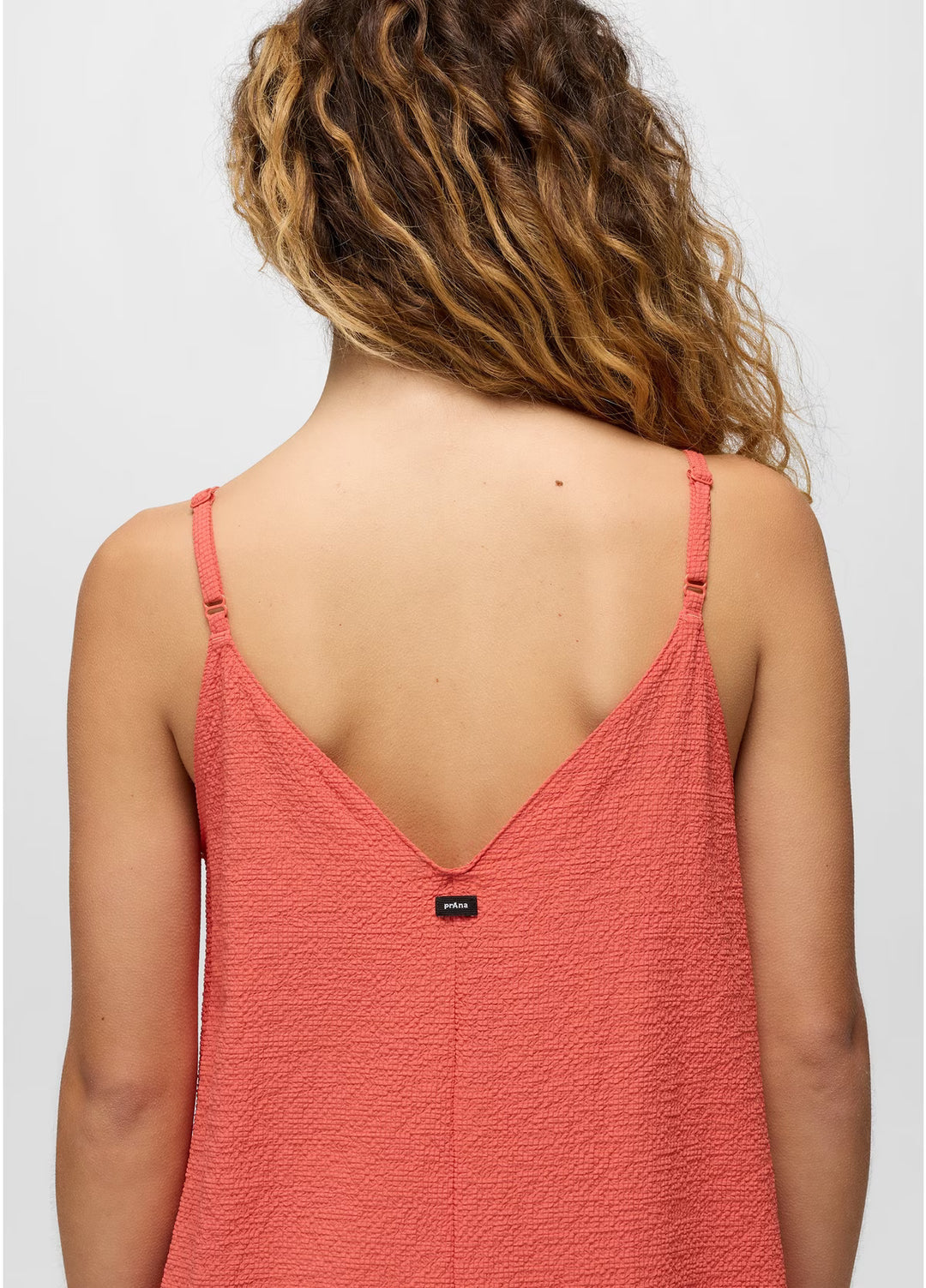 Person wearing a coral pink spaghetti strap top on a plain background