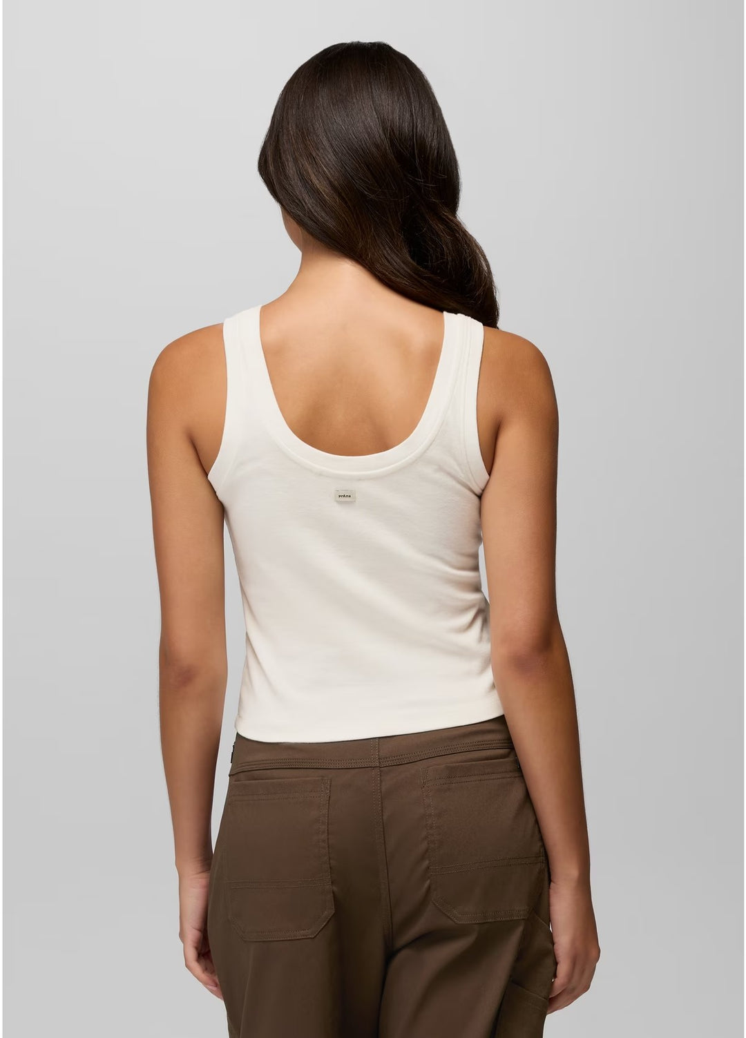 Woman wearing a white tank top and brown pants on a gray background