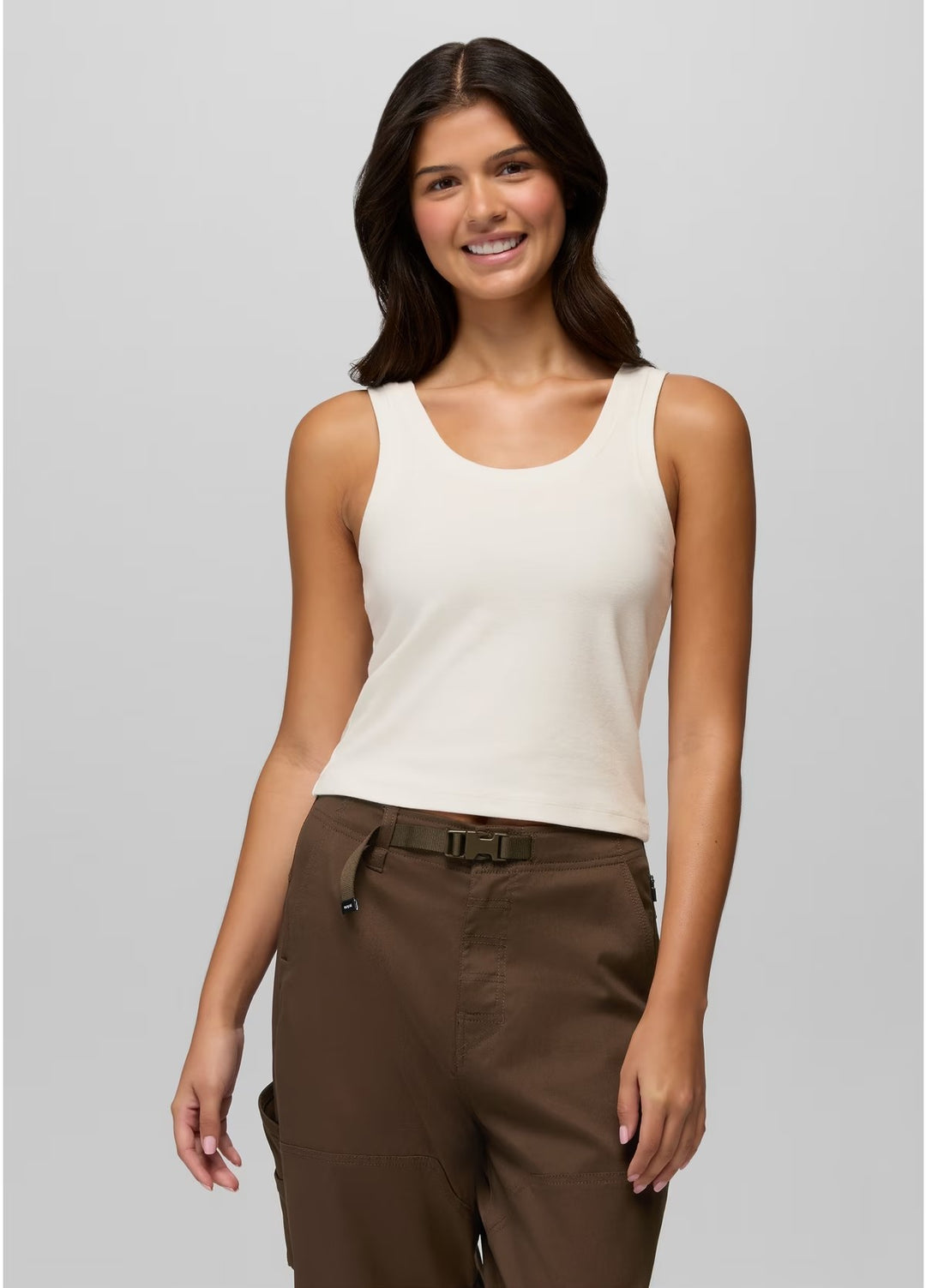 Woman wearing a white tank top and brown pants on a gray background