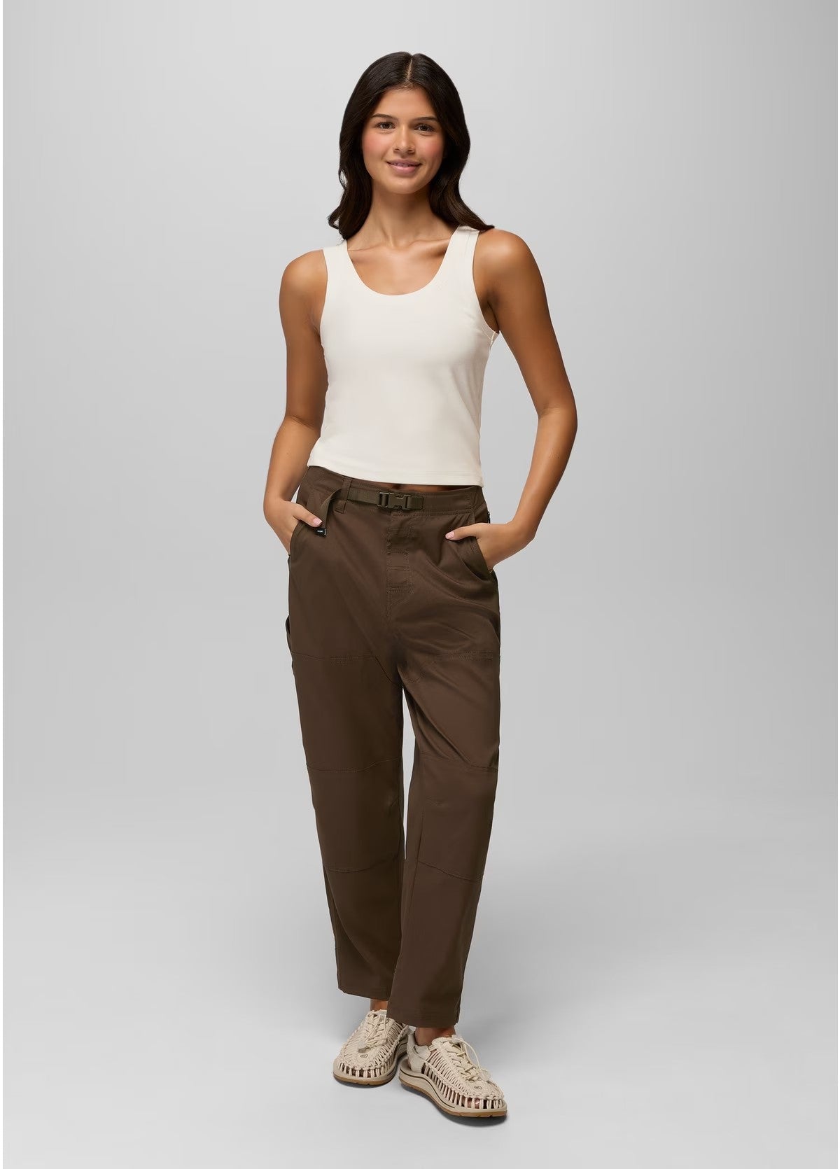 Woman wearing a white tank top and brown pants on a gray background