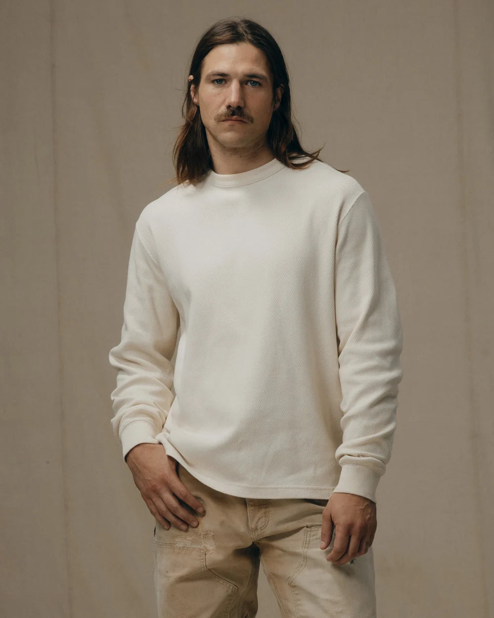 Man wearing a white sweatshirt and beige pants against a beige background