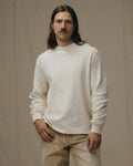 Man wearing a white sweatshirt and beige pants against a beige background