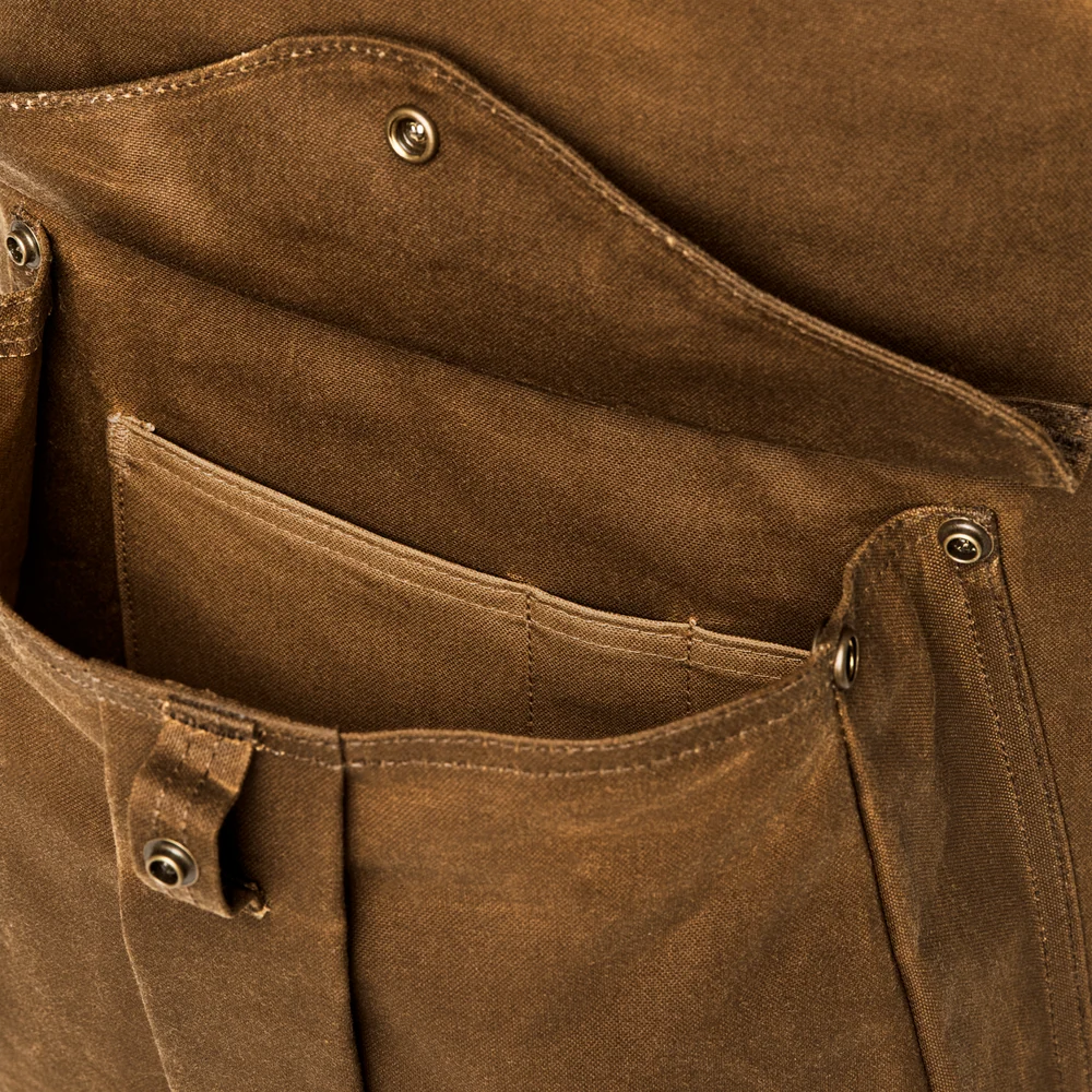 Close-up of a brown canvas utility pocket with metal snap buttons and reinforced stitching.