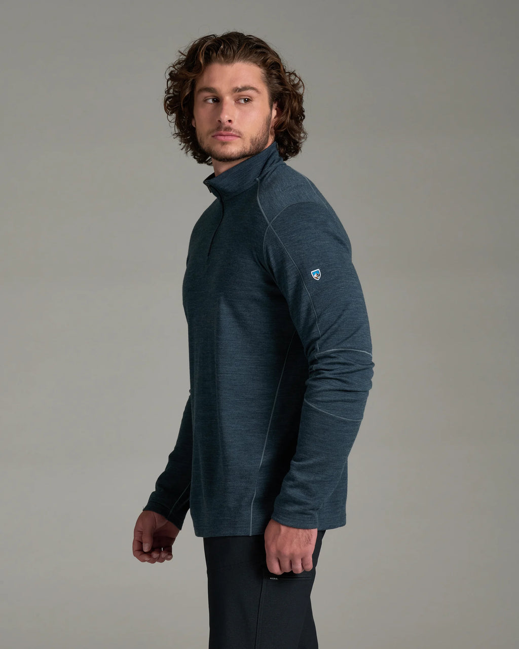 A man wearing a dark slate blue long-sleeve quarter-zip fleece pullover, shown from a side profile against a neutral gray studio background.