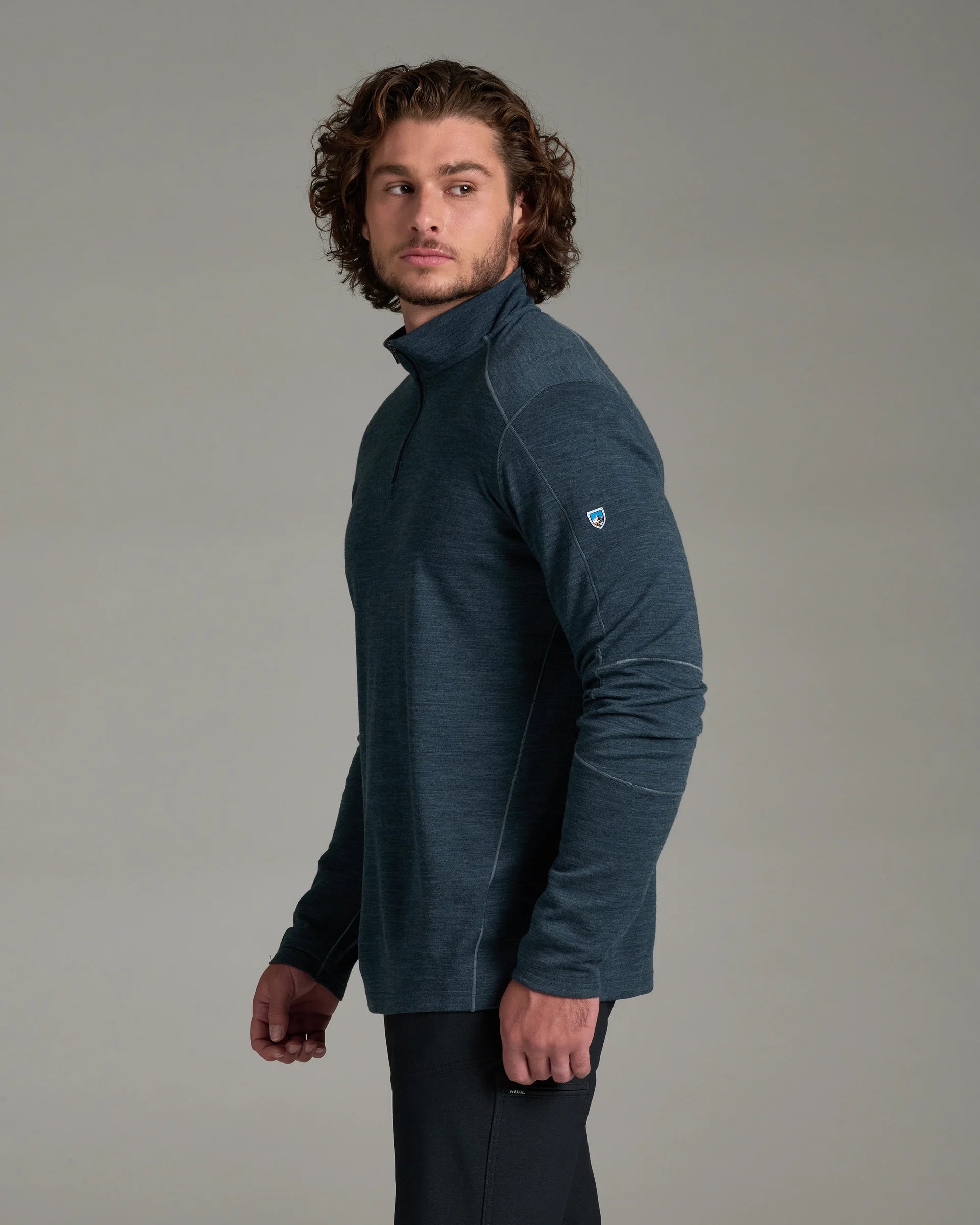 A man wearing a dark slate blue long-sleeve quarter-zip fleece pullover, shown from a side profile against a neutral gray studio background.