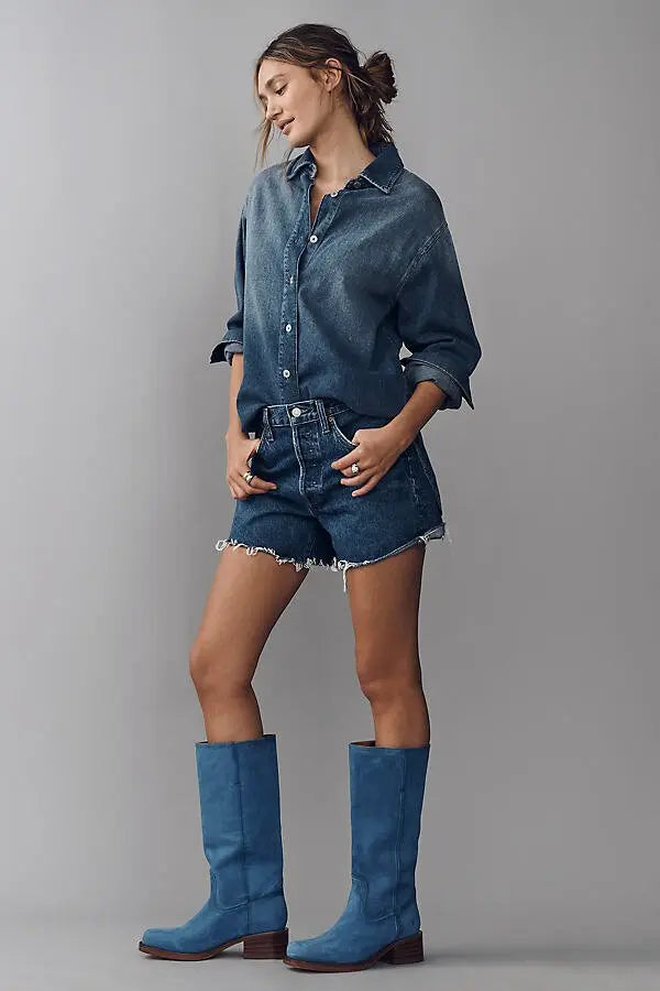 Woman wearing a denim outfit with shorts and boots on a gray background