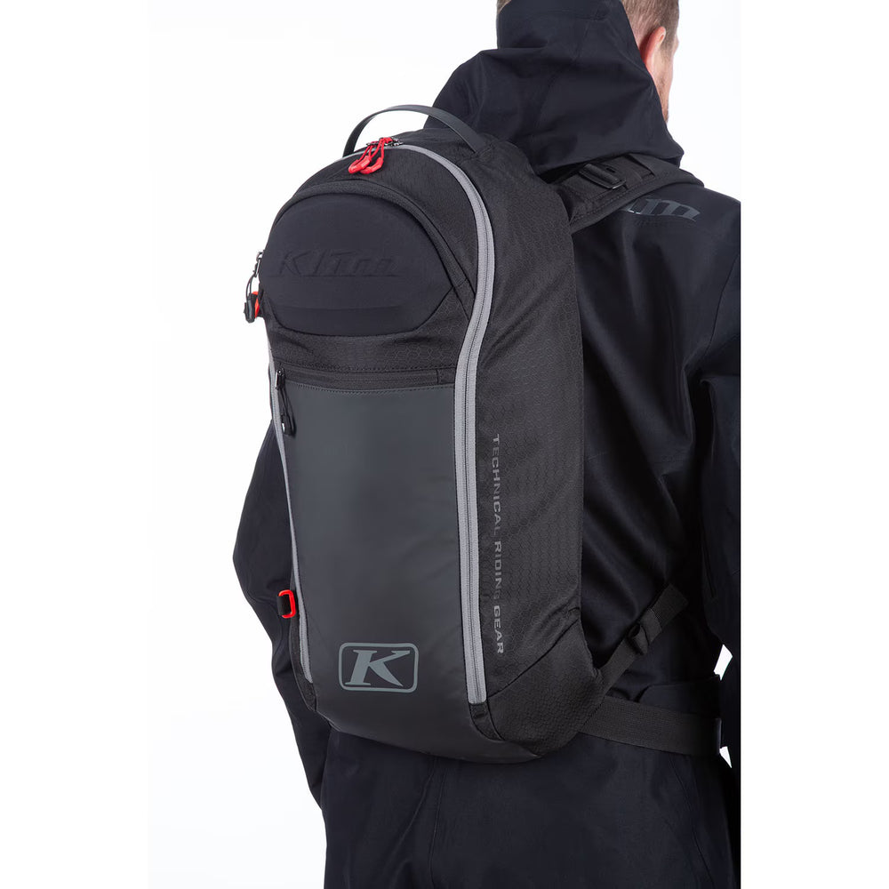 Person wearing a black backpack with Klim logo on a white background