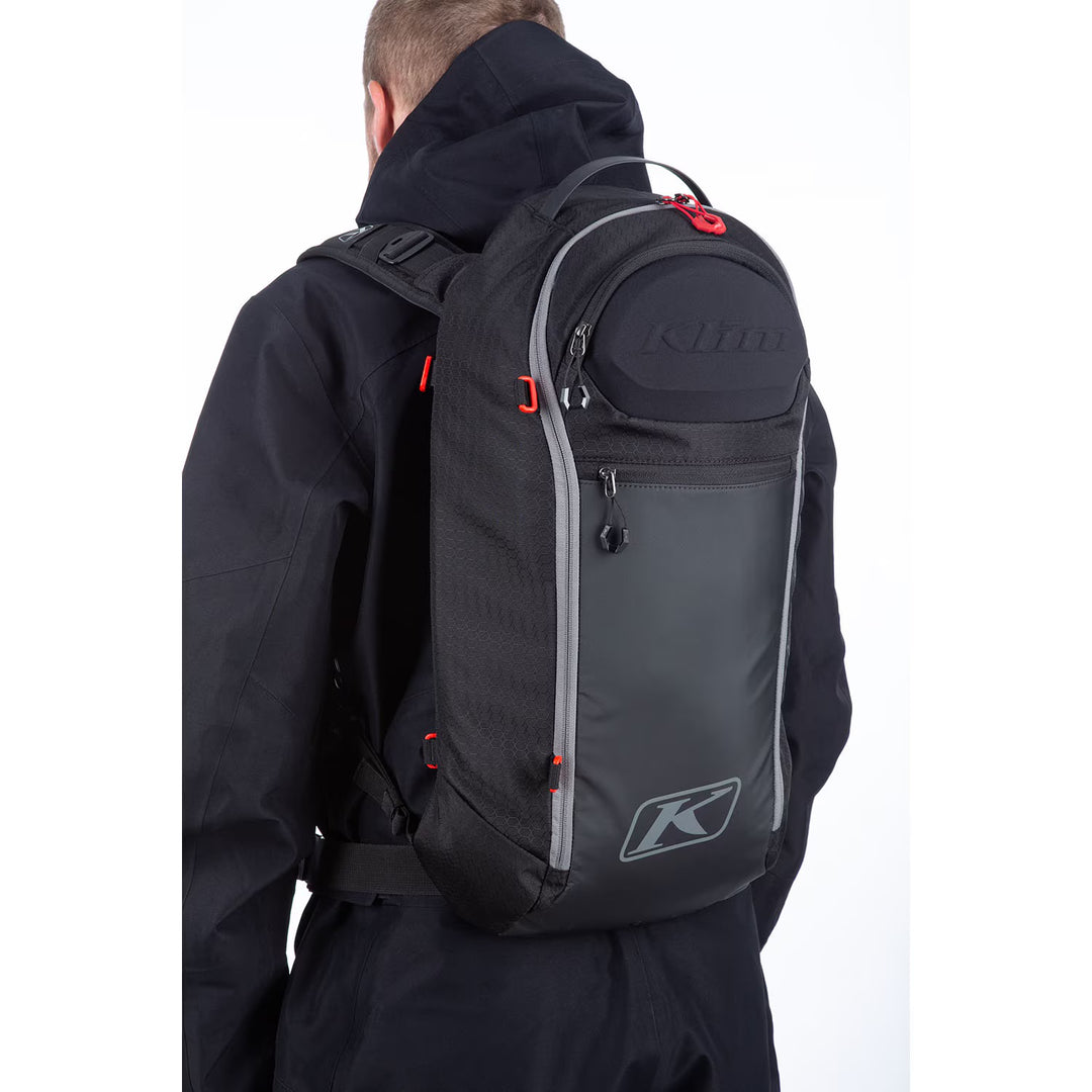 Person wearing a black backpack with Klim logo on a white background