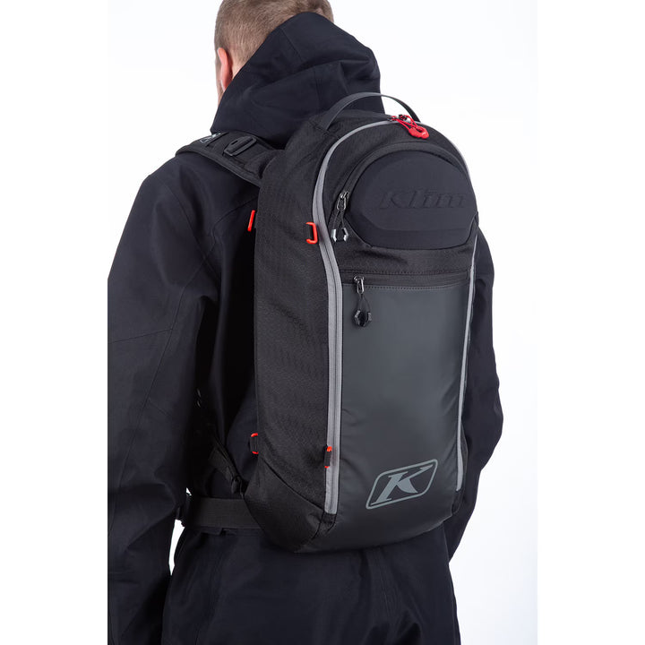 Person wearing a black backpack with Klim logo on a white background